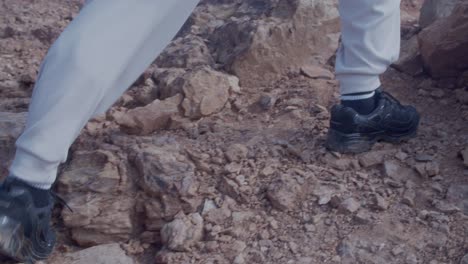 close up on man feet making steps on rock surface of canyon, climbing up