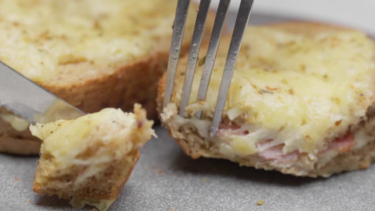 Taglio di un toast con formaggio e prosciutto alla griglia con coltello e forchetta su un piatto