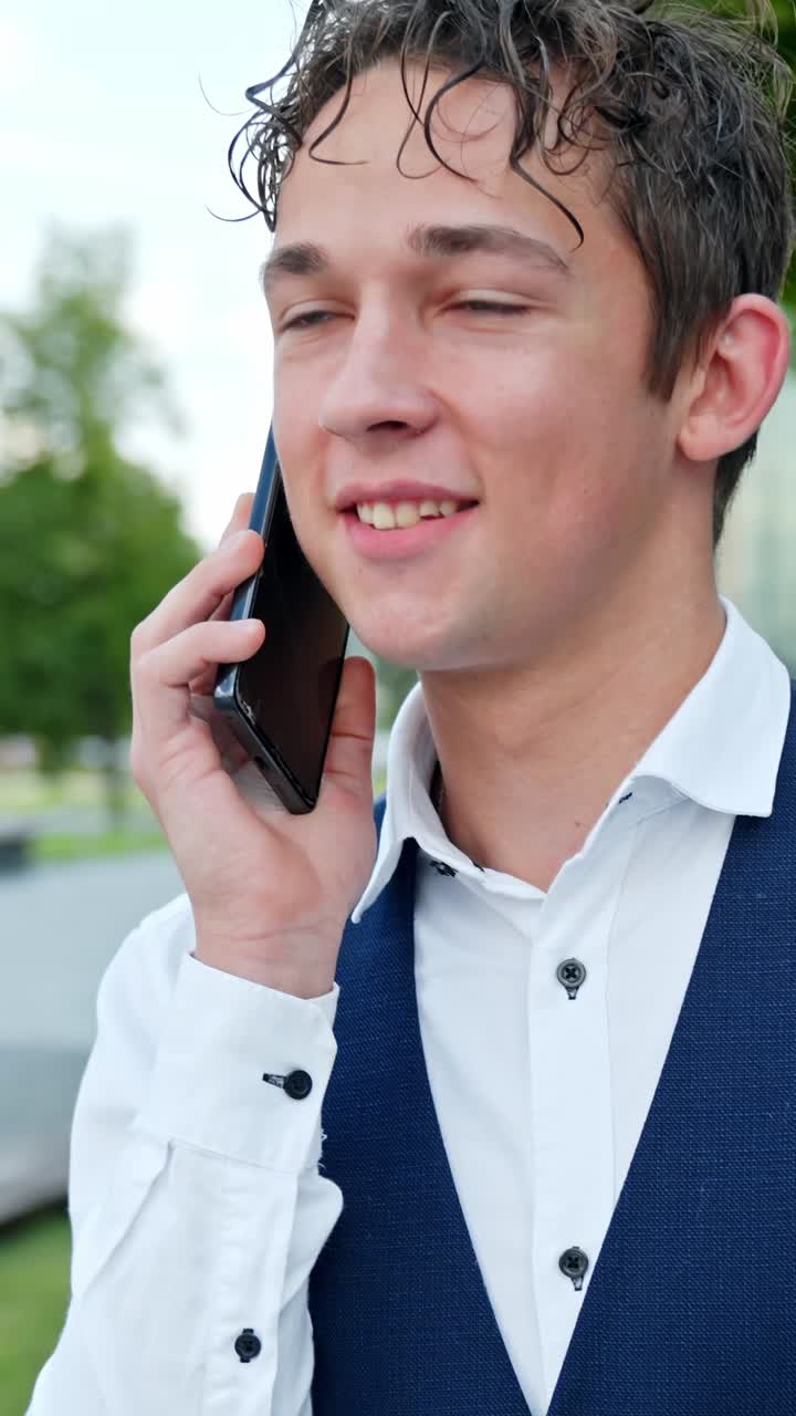 Young man in suit talks happily on phone outside on a bright day