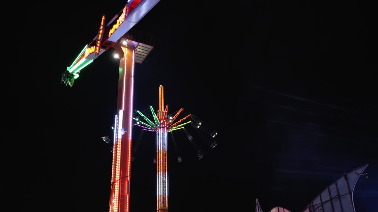 parque de atracciones de 4 km, columpio alto girando y carrusel girando en el fondo por la noche