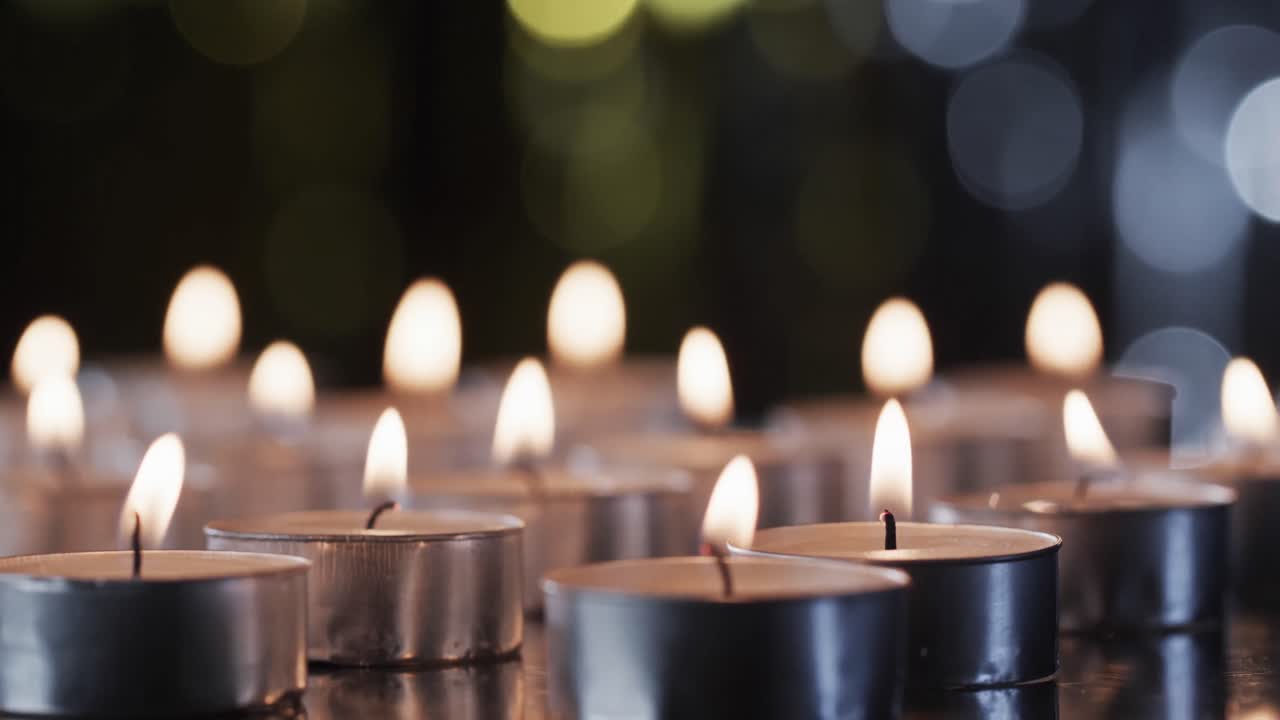 Video di una fila di lumini a candela con fiamme bianche e spazio per il testo con effetto bokeh su sfondo nero