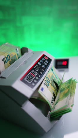 woman puts one hundred euro stack to a money counting machine. side view of the equipment working in the bank. vertical video.