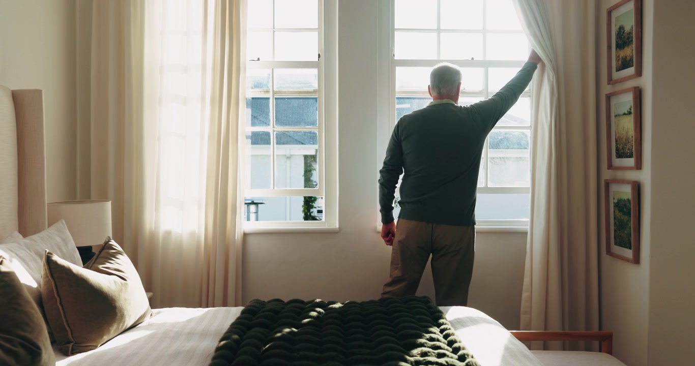 Mature Man Standing by Bedroom Window Looking Outside