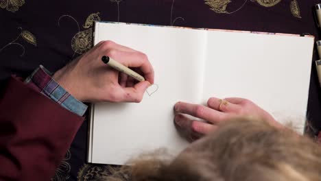 young fine art illustrator graphic designer artist drawing a heart with a fineliner in his sketchbook - close up top shot - 4k