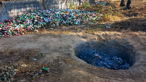 agujero en la tierra quemando basura, botellas y latas de bebidas