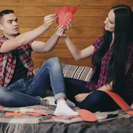 enamored are sitting on the bed and holding red paper hearts in their hands and playing. love story.