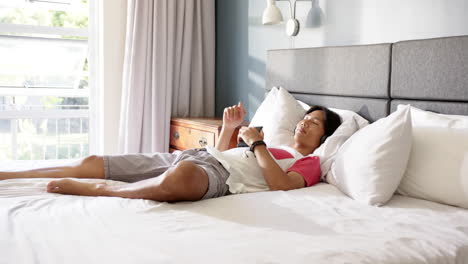 relaxing on bed, asian man using smartphone and enjoying leisure time at home