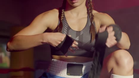 young caucasian sportswoman with braided pigtails wrapping hands with boxing bandages at gym