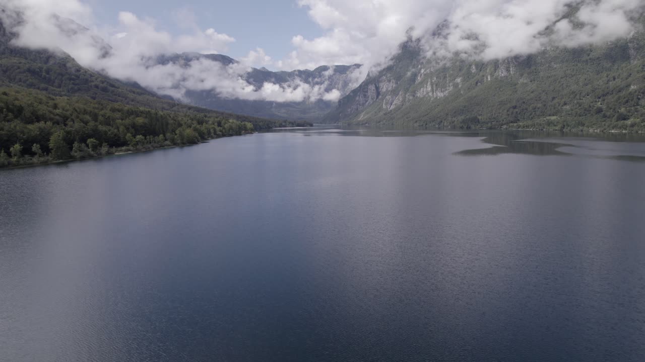video de dron de retroceso ascendente sobre el lago bohinj entre las montañas, cielo despejado con algunas nubes