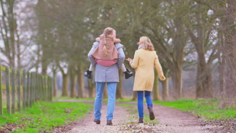 grandfather gives granddaughter piggyback walking through winter countryside with grandmother