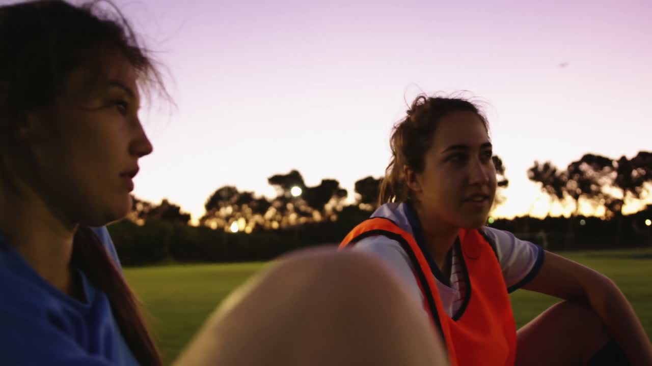 Squadra di calcio femminile seduta a terra che parla sul campo da calcio. 4k