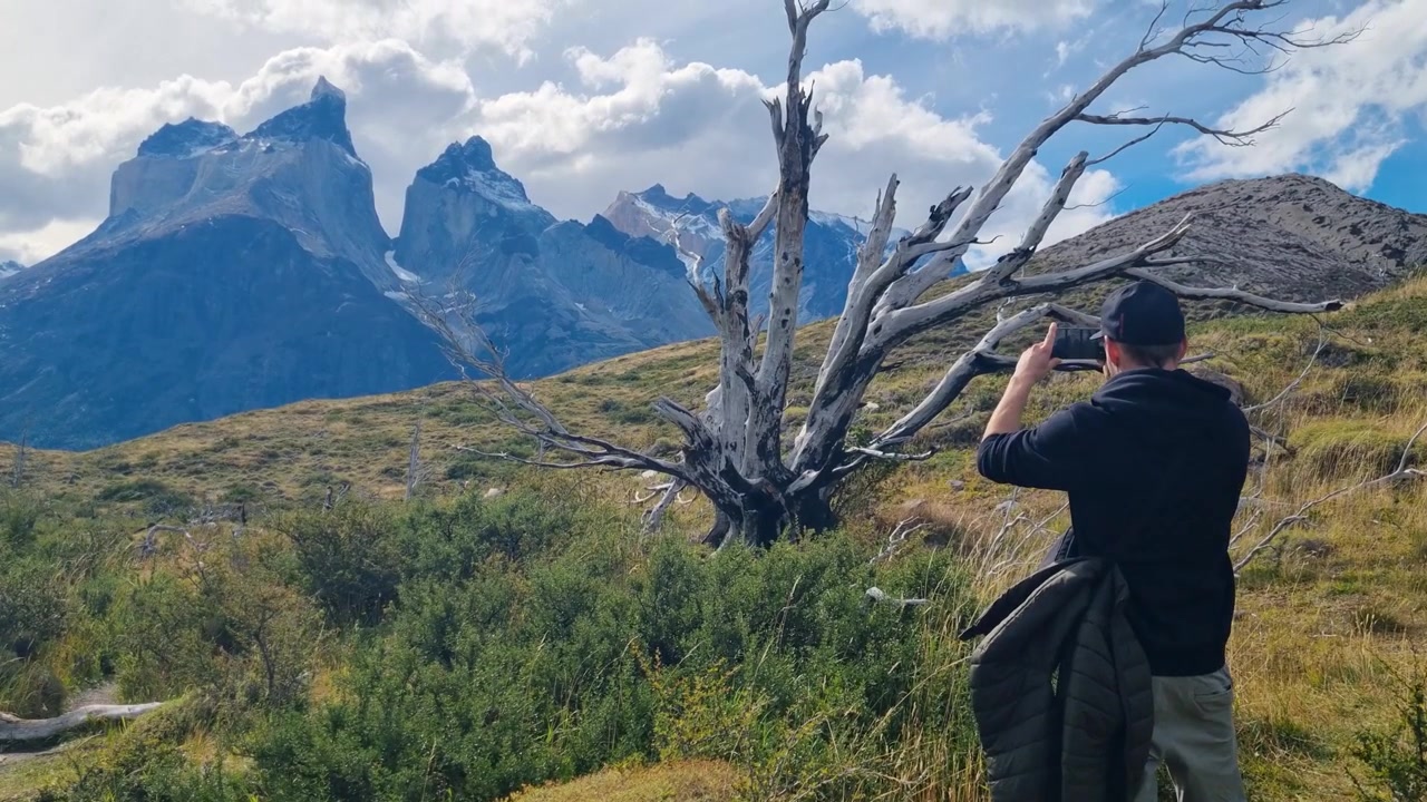 Escursionista che fotografa le splendide montagne del Parco Nazionale Torres del Paine mentre fa trekking attraverso il mozzafiato paesaggio patagonico con uno smartphone, Cile.