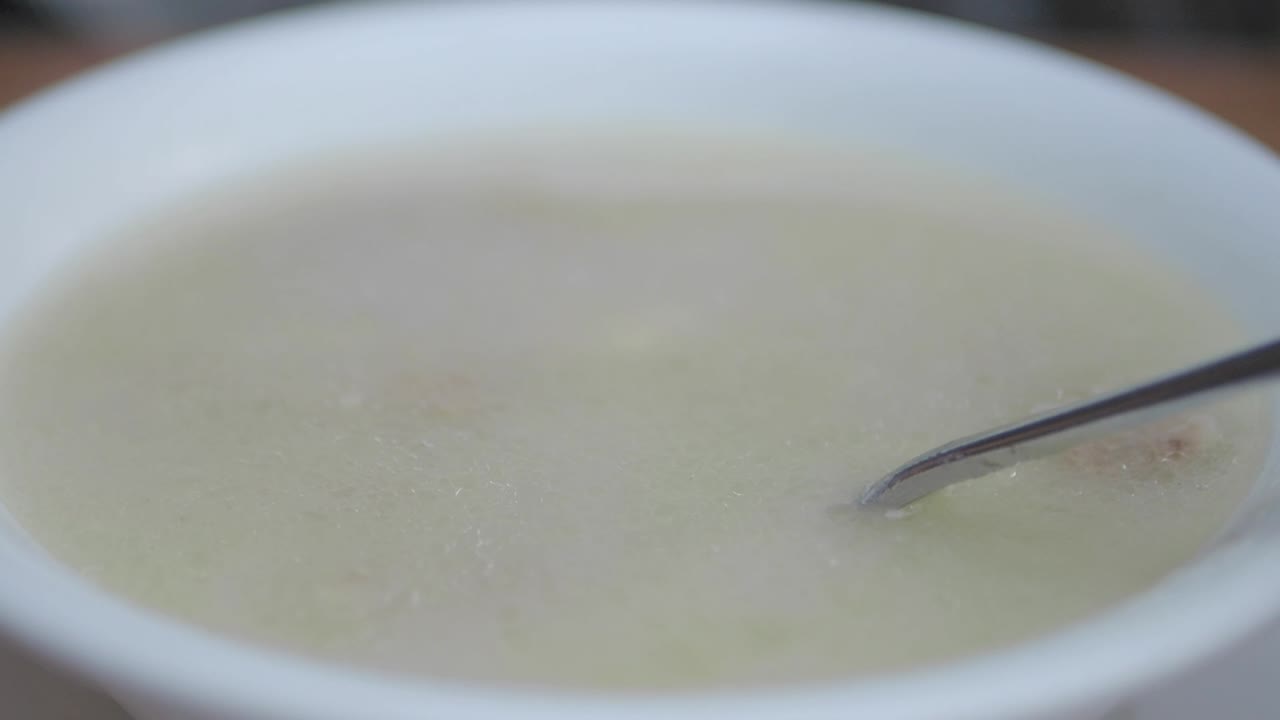 Close-up of light-colored soup in a white bowl with a spoon