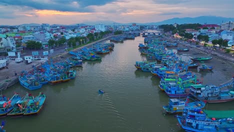 Drone-view-basket-boat-moving-through-fishing-boats-are-nailing-side-by-side-on-the-Ca-Ty-river,-Phan-Thiet-city,-Binh-Thuan-province,-central-Vietnam