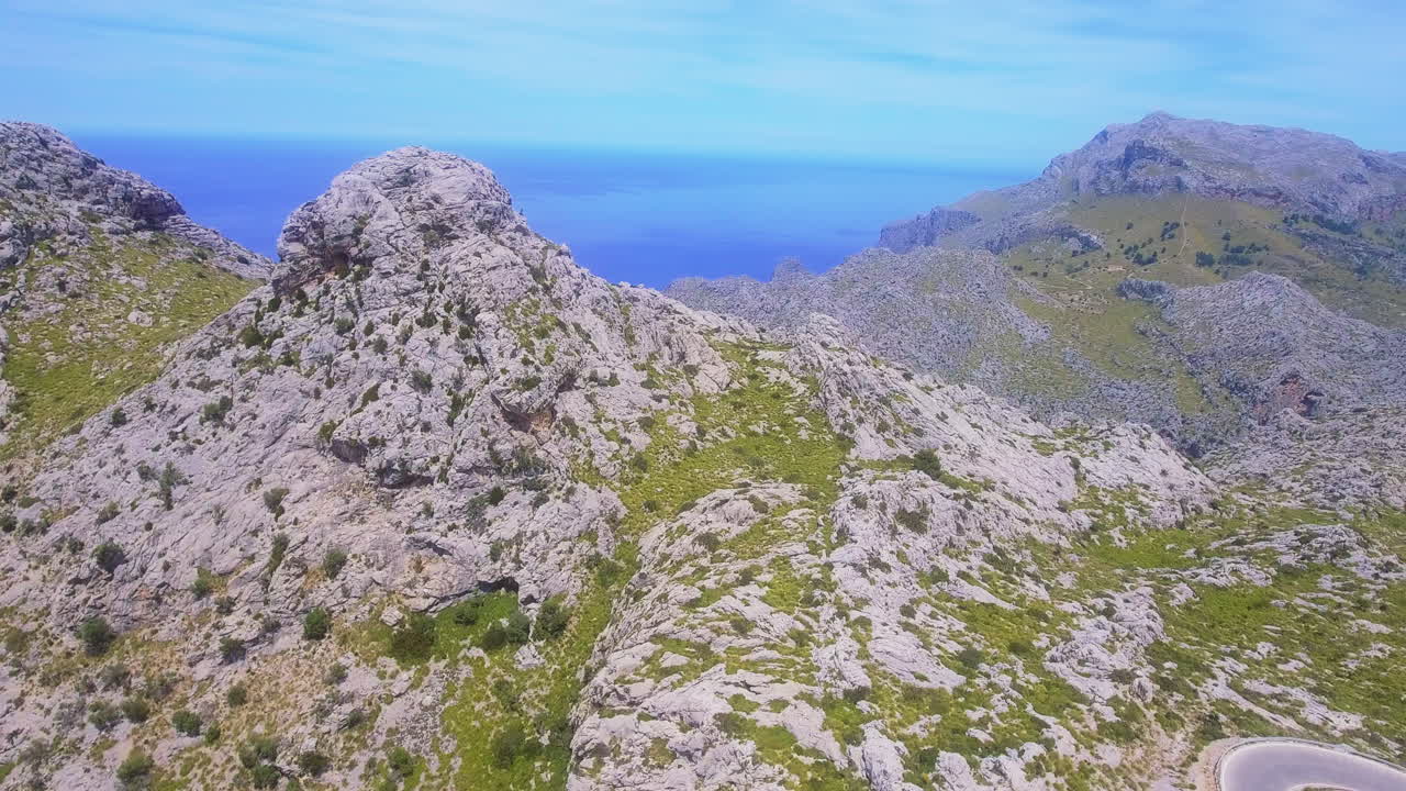 Vista aerea sorvolando le montagne rocciose con vegetazione verde e il mare visibile in lontananza a Maiorca