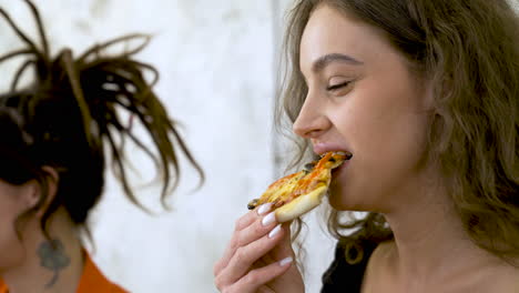 close up of a young woman eating slice of pizza with friends at home