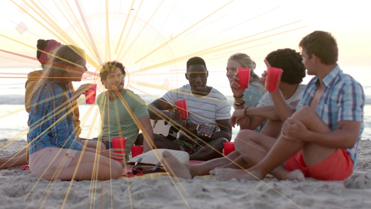 7 friends sitting on beach one raising red cups starting toast guitarist playing flare pulsing ads