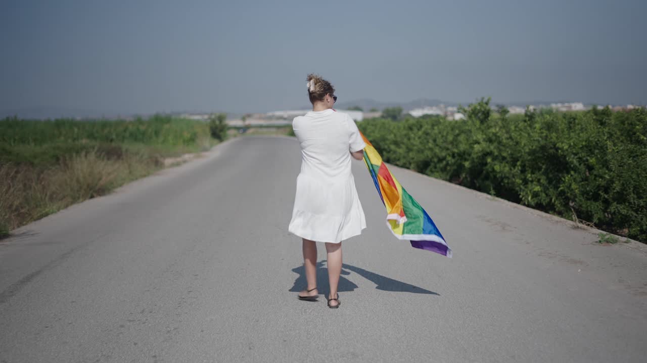 Woman walking with a rainbow flag on a country road