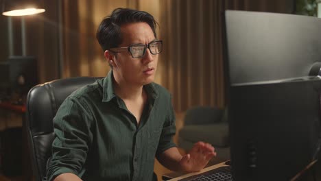 tired asian male works his personal computer. he works at night