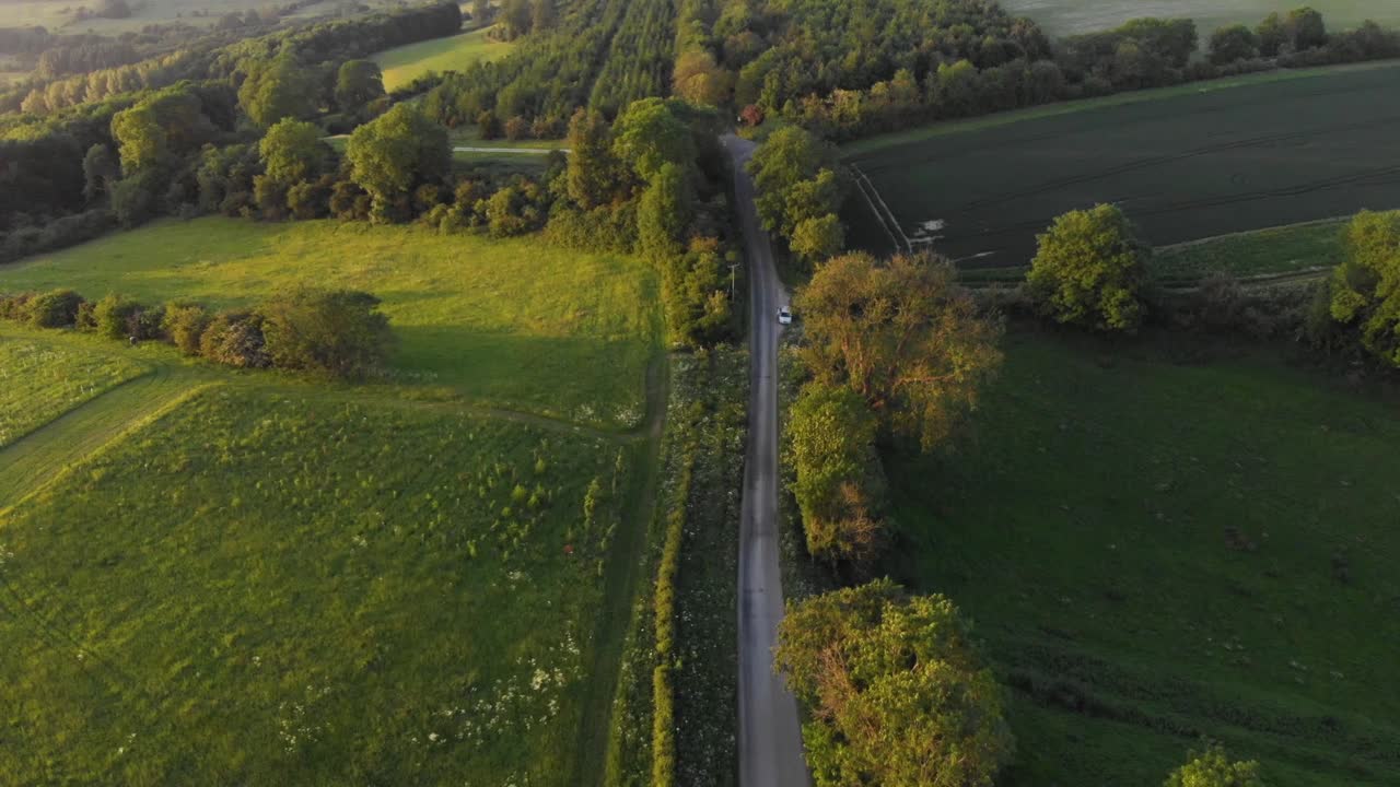 밝은 주황색 빛으로 일몰 동안 녹색 시골에 있는 영국 시골길의 공중 영화
