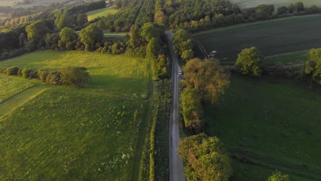 aerial cinematic shot of english country road in green countryside during sunset with bright orange glow