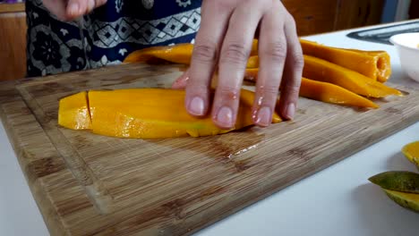 manos cortando fruta fresca de mango con un cuchillo en una tabla para cortar madera, de cerca