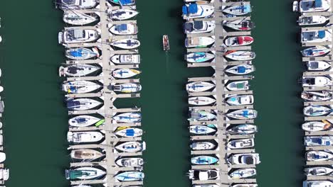 top-down drone view of boats docked in oceanside harbor, and one boat pulling out of the harbor.