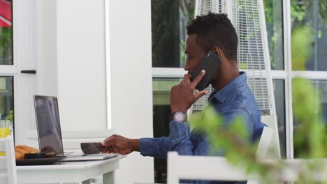 hombre de negocios afroamericano usando una computadora portátil y hablando en un teléfono inteligente en un café