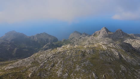 flying over rigged mountains with vegetation and the sea in the background with clouds above at sa calobra, mallorca, spain