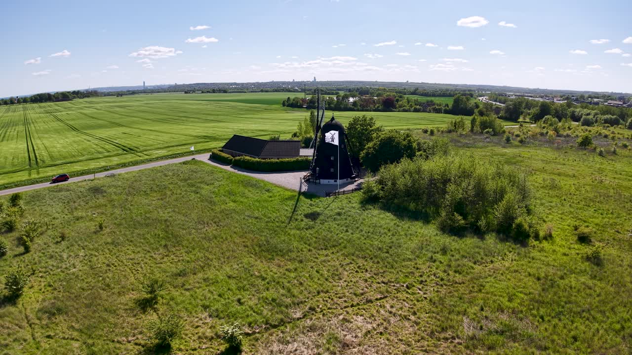 Aerial drone footage of Ega Mill in Denmark surrounded by open farmland and green fields under a bright summer sky, showcasing rural countryside scenery