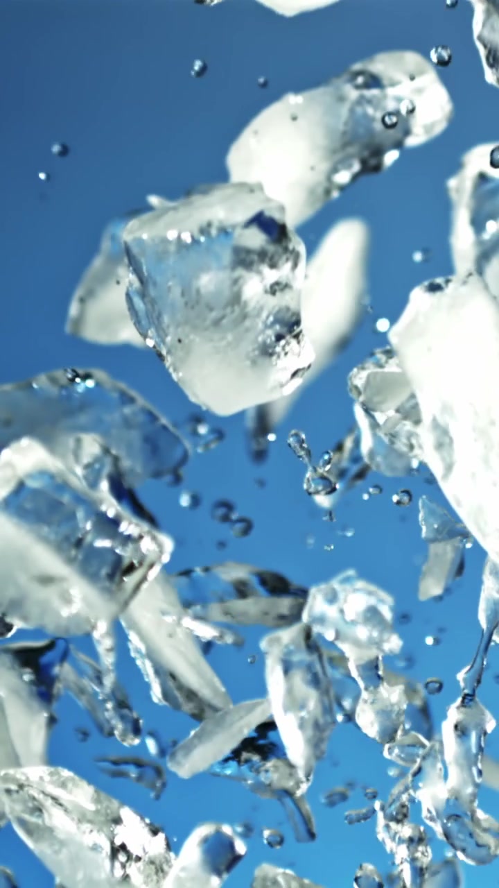 Cubetti di ghiaccio e goccioline d'acqua che cadono al rallentatore su sfondo blu