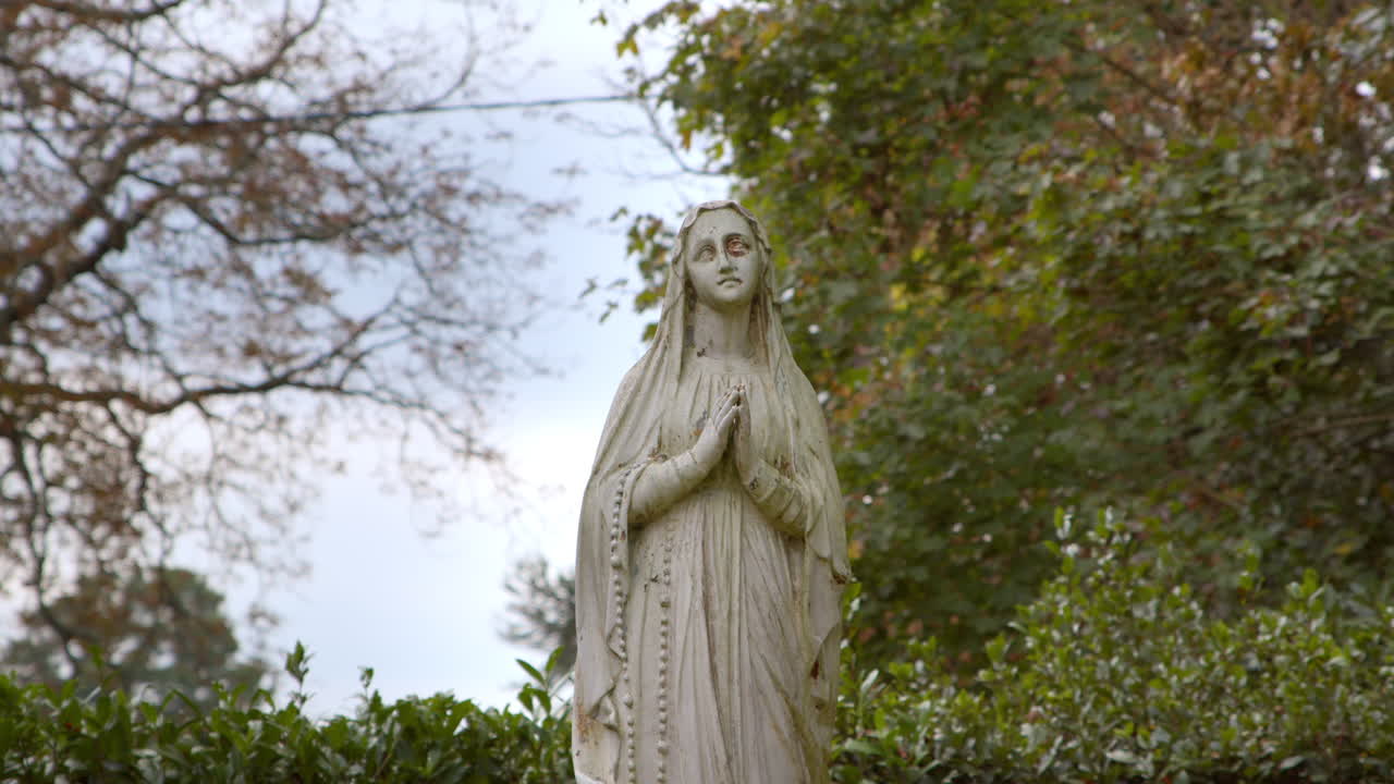 Statua antica della Vergine Maria che prega su uno sfondo naturale. Inquadratura fissa