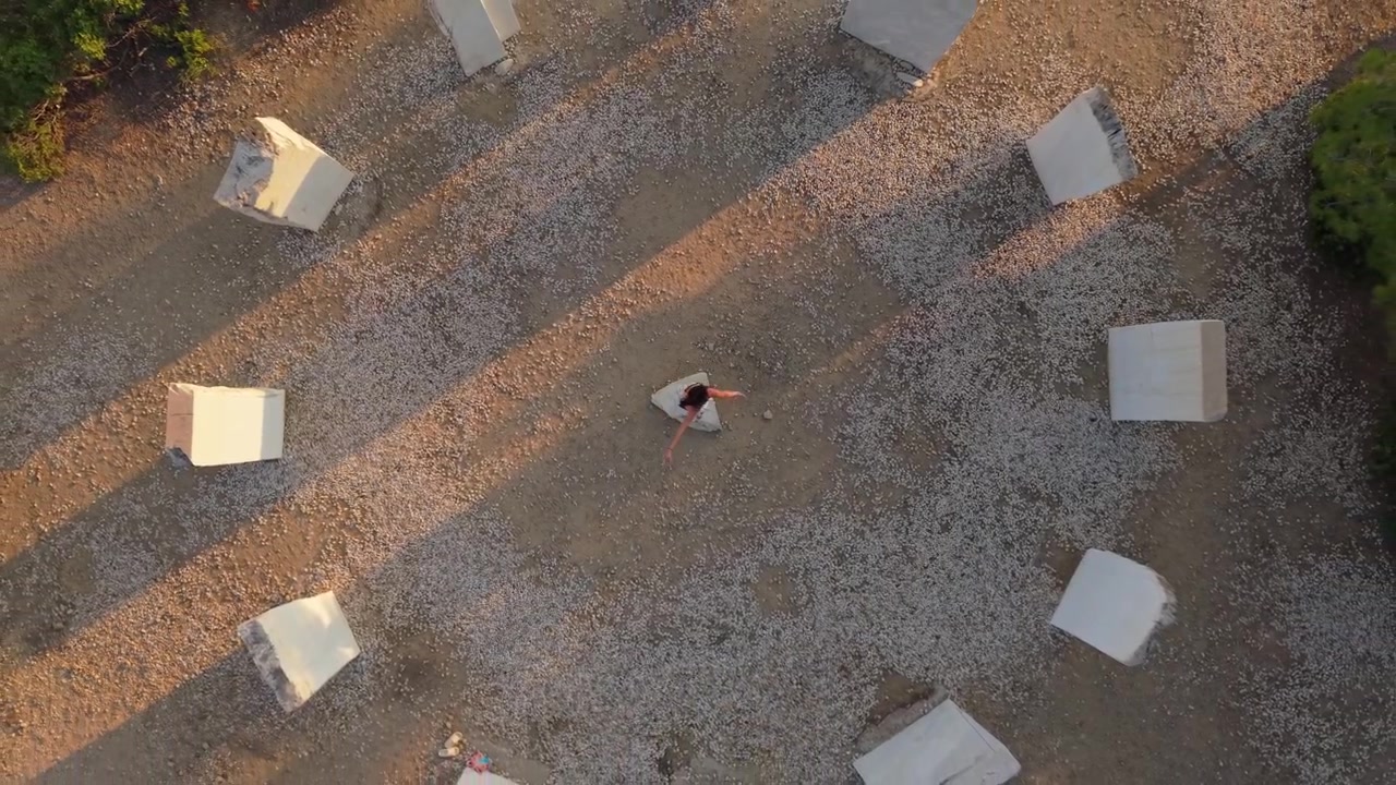 Vertical drone shot of a woman spinning in harmony at the center of the Crown of Limenaria in Thassos, emphasizing symmetry, motion, and balance.