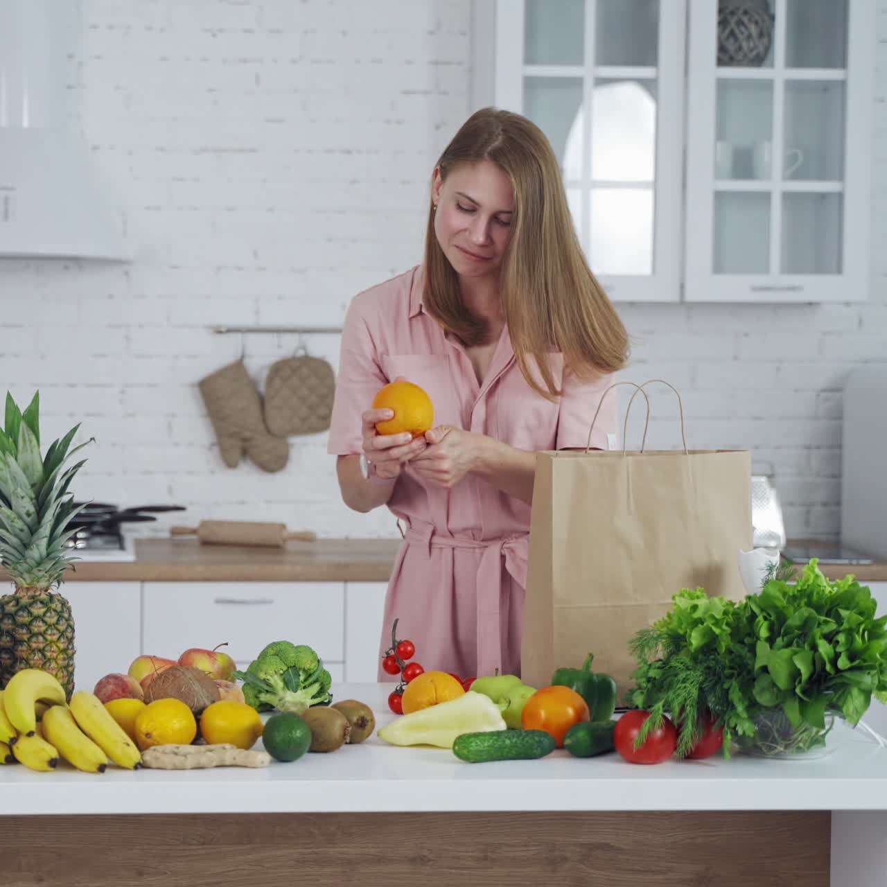 Joyful woman taking out fresh fruit from paper bag in the kitchen. Organic fruit and vegetableson the table and beautiful female indoors. Healthy lifestyle.