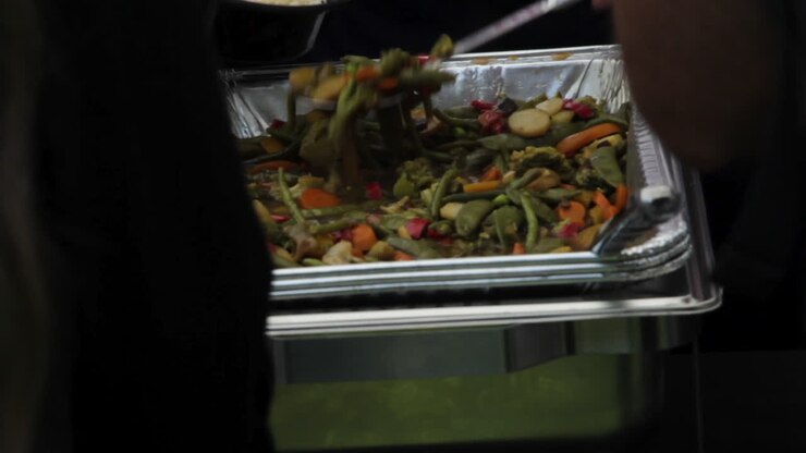 Bakke med catering-ristede grøntsager på et travlt buffetbord med folk der forsyner sig
