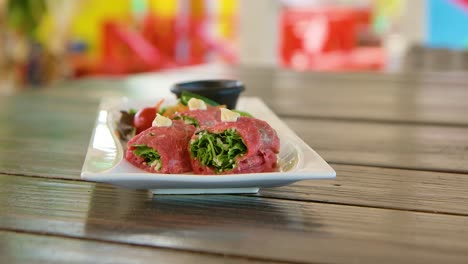 Slow-orbit-of-carpaccio-bites-appetizer-on-long-white-plate,-colorful-background