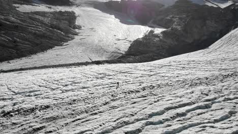 aerial view of a hiker walking across the ice of the allalin glacier near saas-fee in valais, switzerland on a sunny day in the swiss alps