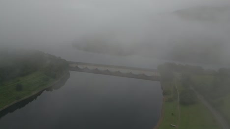 view of ladybower reservoir bridge in misty morning with cloudy sky surrounded by green hills