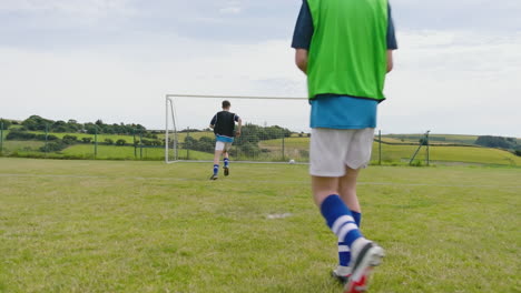 male soccer players shooting at goal one after another and running after ball on pitch, copy space