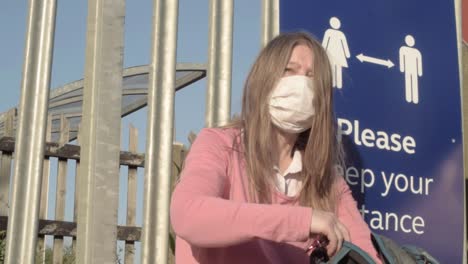 Woman-wearing-mask-looking-in-bag-near-to-social-distancing-sign-medium-shot