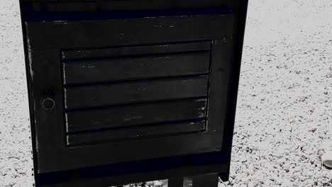 black and white of an old fashion newspaper box painted black without a newspaper