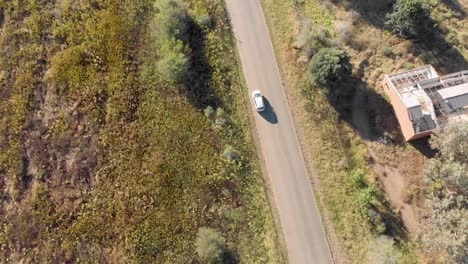 aerial following a silver car travelling on an open road with fields on both sides