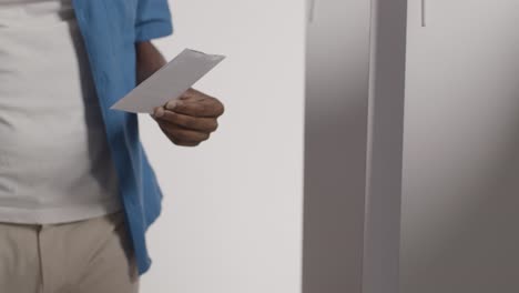 close up of man in booth filling in ballot paper in american election casting vote into ballot box