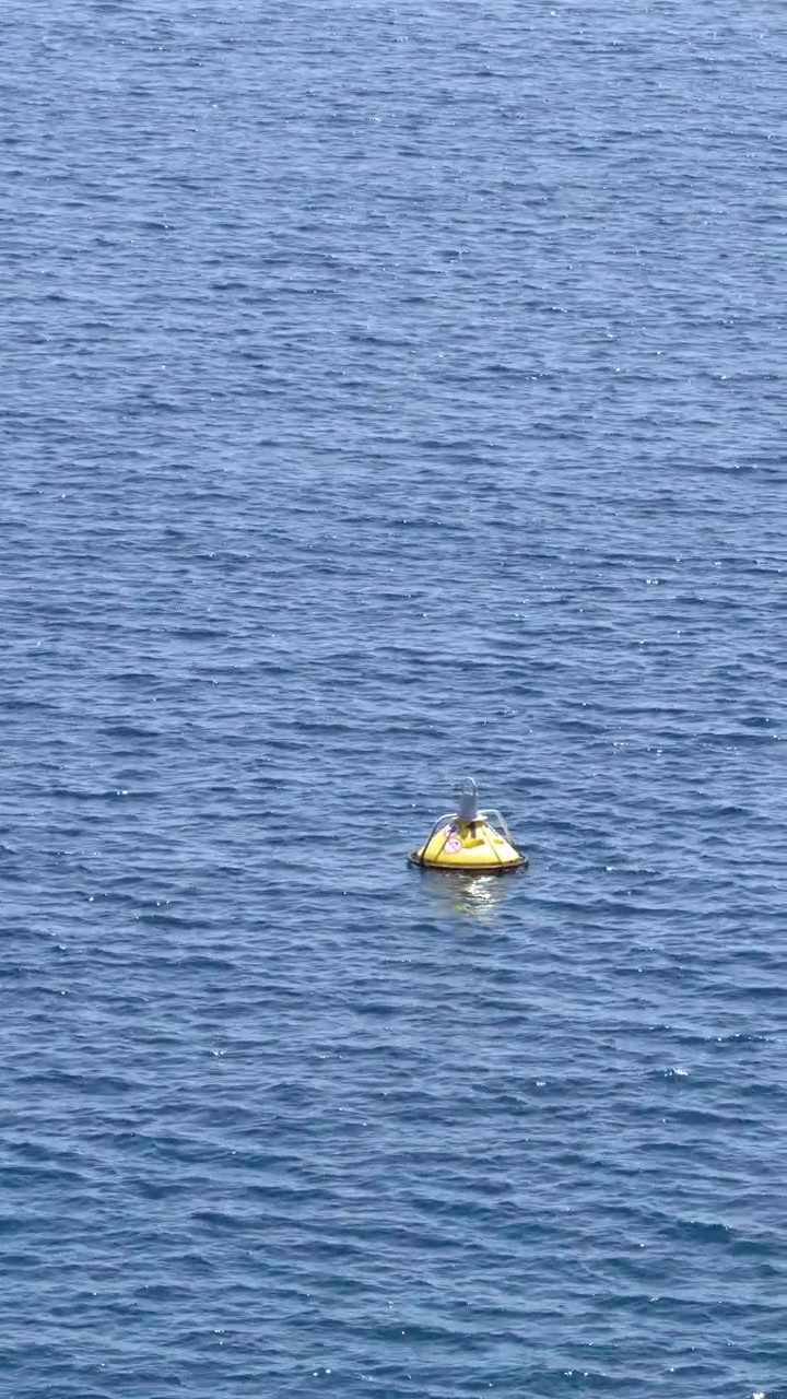 A yellow navigation buoy floats on calm blue sea water under bright natural sunlight.