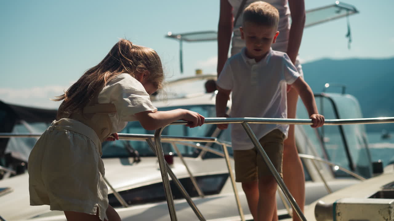 la niña baja cuidadosamente por la escalera del barco de motor mientras la madre y el niño esperan en el puente levadizo para aterrizar en el puerto de la ciudad. la hermana mayor muestra a su hermano aterrizando desde el yate