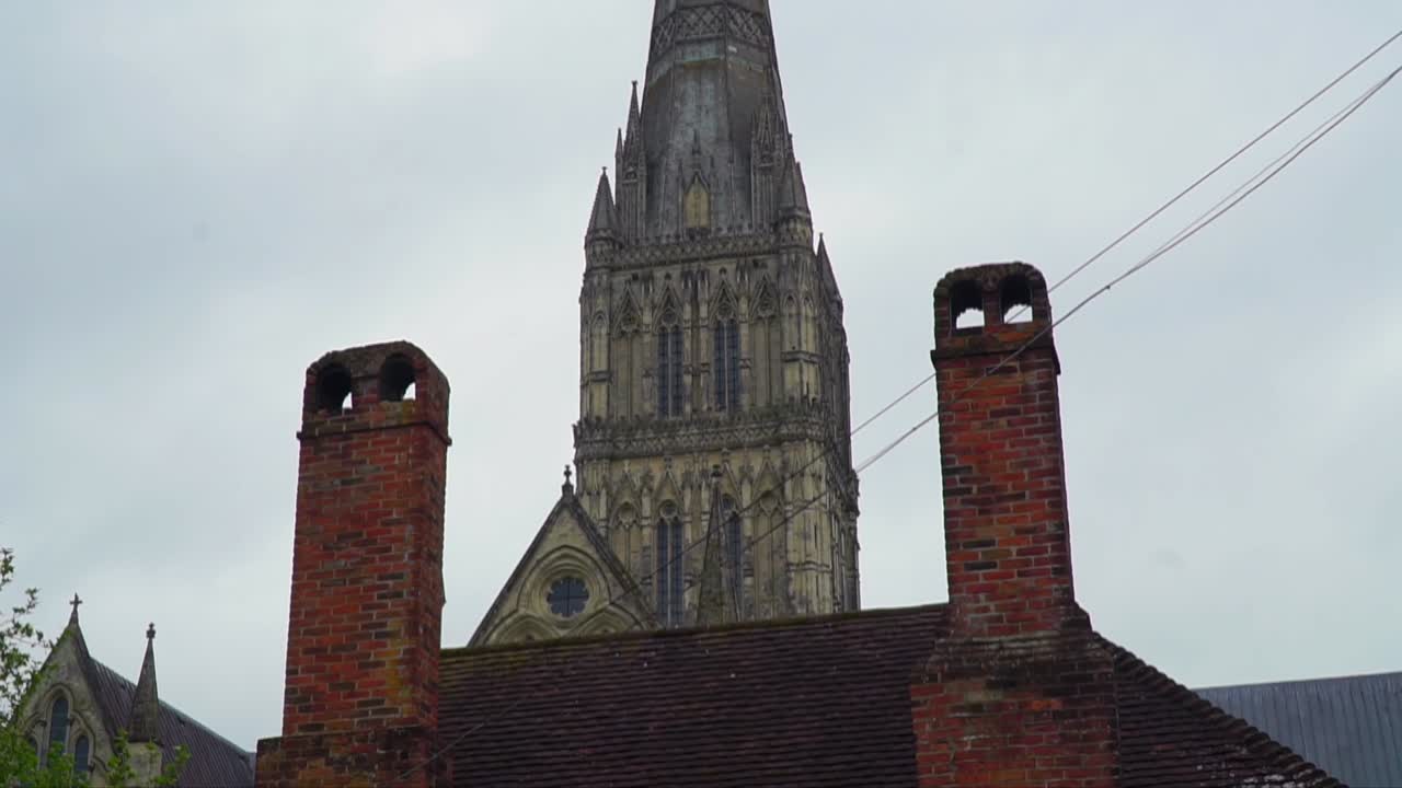 The Gothic spire of Salisbury Cathedral stands tall behind old red brick chimneys in Salisbury, Wiltshire, showcasing England’s architectural contrasts and heritage charm.