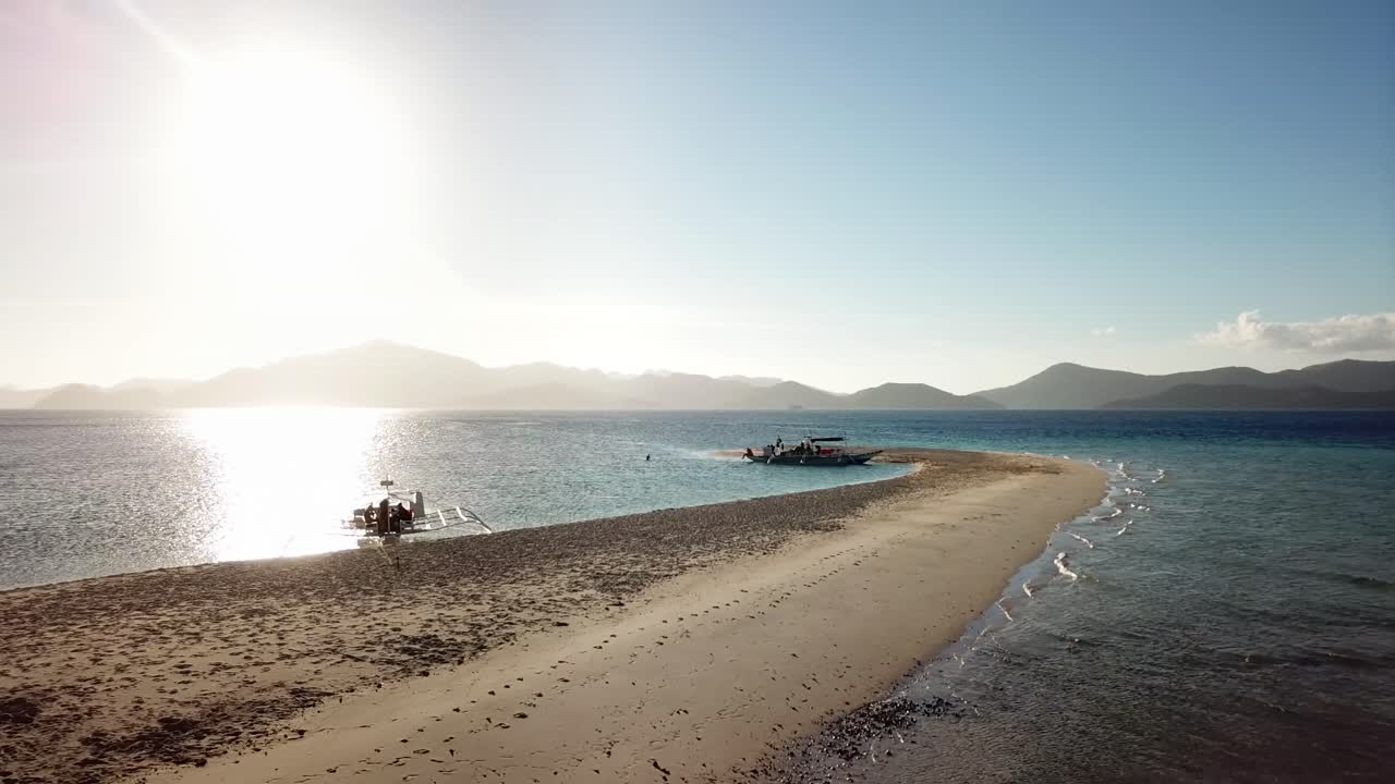 Aerial drone shot of beautiful sunset over the ocean, sandy beach and boats at an island in Palawan, Philippines.