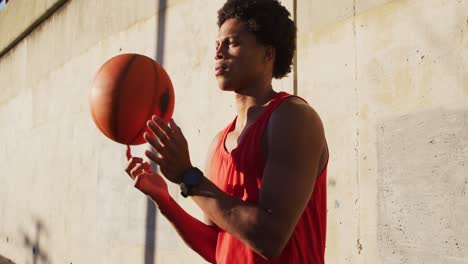hombre afroamericano en forma haciendo ejercicio al aire libre en la ciudad, equilibrando el baloncesto giratorio en la punta del dedo