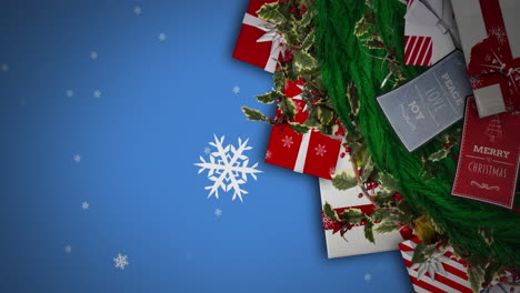 snowflakes falling over christmas wreath decoration and gifts against blue background