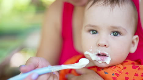 caring mom feeding her little baby boy from a spoon. nice kid distracts a little and watches aside and then takes the spoon.